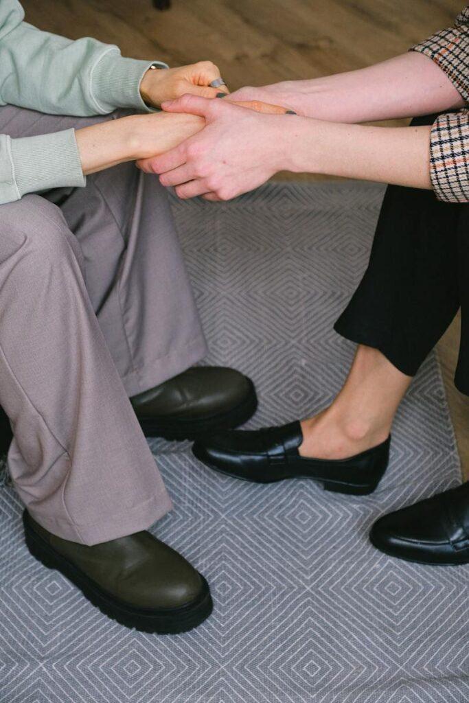 From above of crop unrecognizable psychotherapist holding hands of woman while interacting during counseling on carpet
