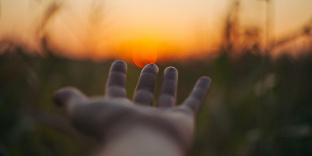 selective focus photo of person laying hand over the sunset