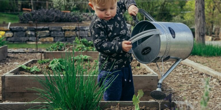 boy in black and white long sleeve shirt standing beside gray metal watering can during daytime