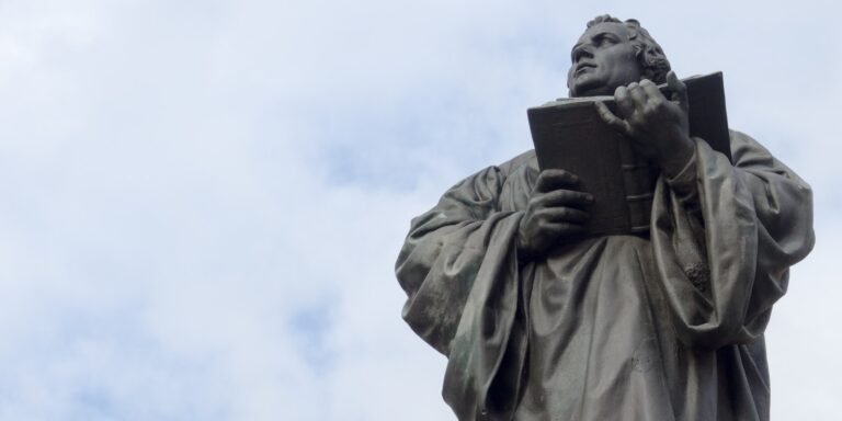 man holding book statue under white clouds during daytime